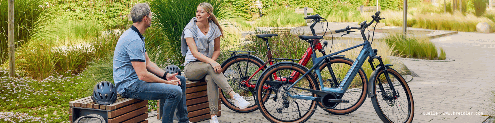 Zwei Personen sitzen auf einer Bank und unterhalten sich in einem Park mit Fahrrädern