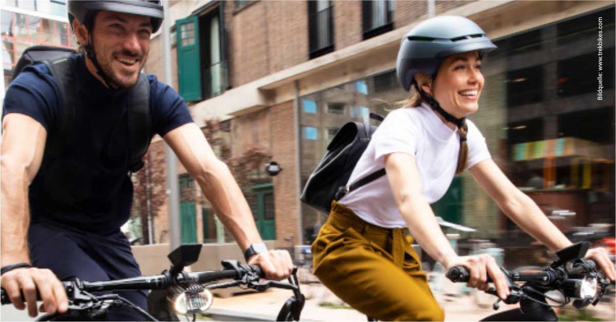 Zwei Menschen fahren lächelnd Fahrrad durch eine städtische Umgebung