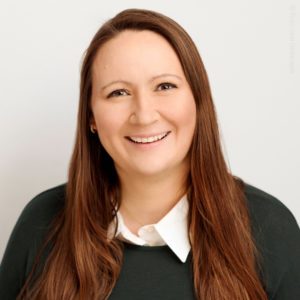 Eine Frau lächelt freundlich vor einem hellen Hintergrund